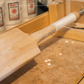 Wooden cricket bat with handle being strung on a wooden surface, with 'Trogon' branding visible.