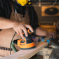 Person sanding a wooden Trogon cricket bat with a sander, wearing a yellow helmet and apron.