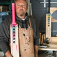 Man holding a TROGON cricket bat in a workshop setting
