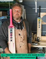 Man holding a TROGON cricket bat in a workshop setting