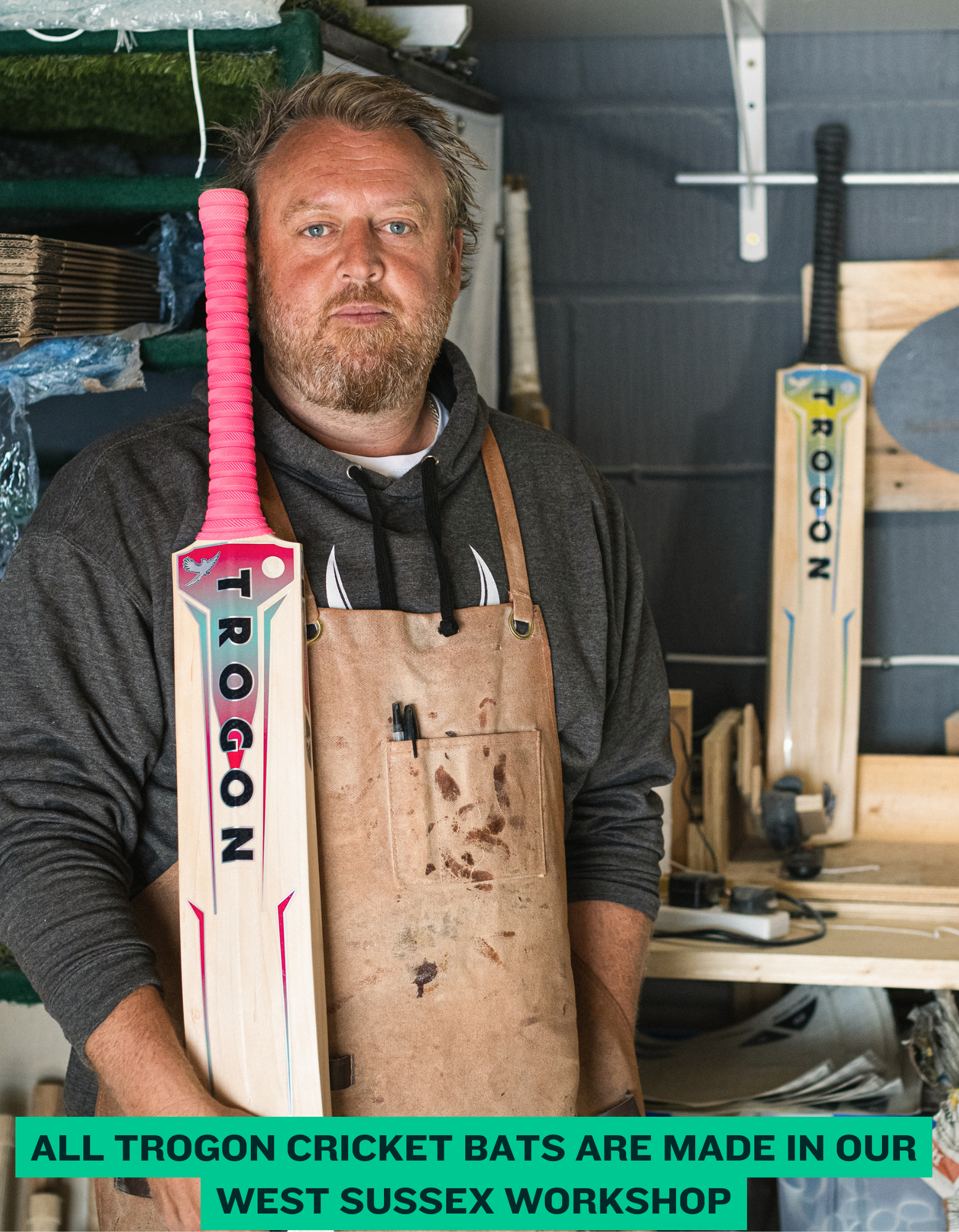 Man holding a TROGON cricket bat in a workshop setting